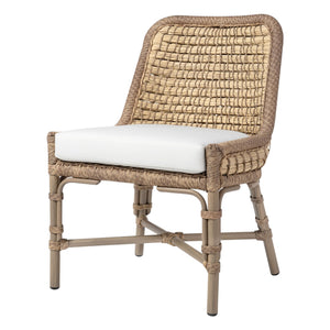 The PALECEK Capitola Outdoor Side Chair in Nit Witty Sea Salt features woven synthetic seagrass, a light cushion, wood legs, and an arched backrest, shown against a white background.