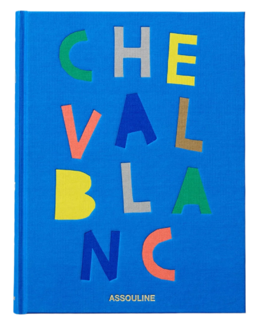 A blue book cover features colorful letters spelling "CHEVAL BLANC" vertically and horizontally, reflecting luxury hospitality, with the brand name "Assouline" at the bottom.