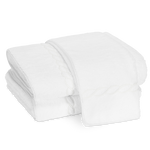A stack of white bath towels from the Matouk Classic Chain Bath Collection, featuring a subtle decorative border and crafted from Cairo cotton terry, neatly folded on a plain white background.