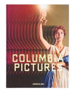 A book cover titled "Columbia Pictures" by Assouline celebrates 100 Years of Cinema, featuring a woman holding a torch against a textured background with the names "Columbia Pictures" and "Assouline" at the bottom, evoking a rich film history.