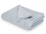 The Costa Mesa Blanket Collection by Matouk is displayed, featuring a neatly folded light grey blanket with a soft knitted texture on a white background.