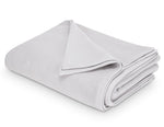 The Costa Mesa Blanket Collection by Matouk features a neatly folded light gray blanket with a soft knitted texture, shown on a white background.