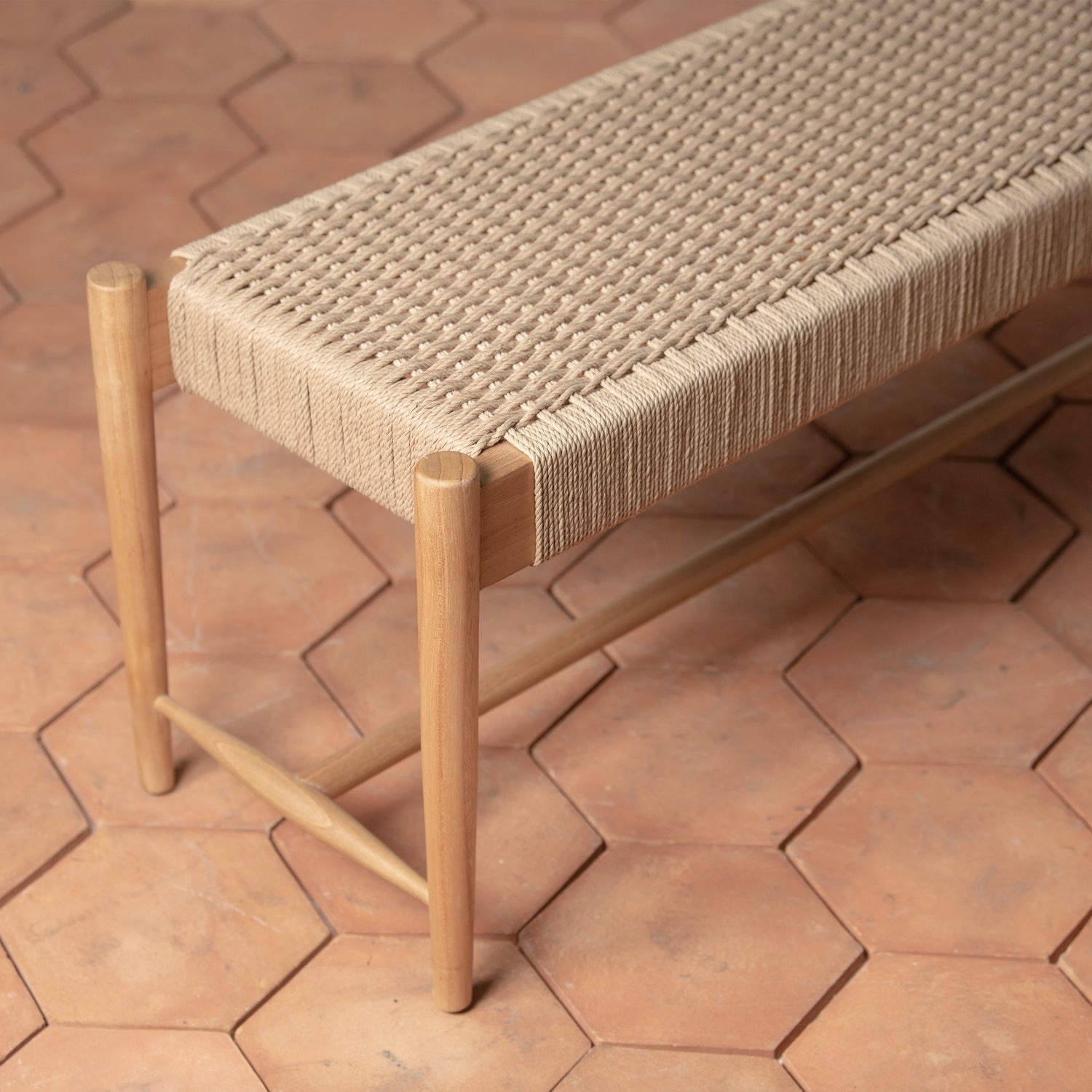 The Ingrid Woven Bench by Selamat features a hand-woven seat and sits atop large hexagonal terracotta tiles, blending natural charm with timeless Scandinavian design.
