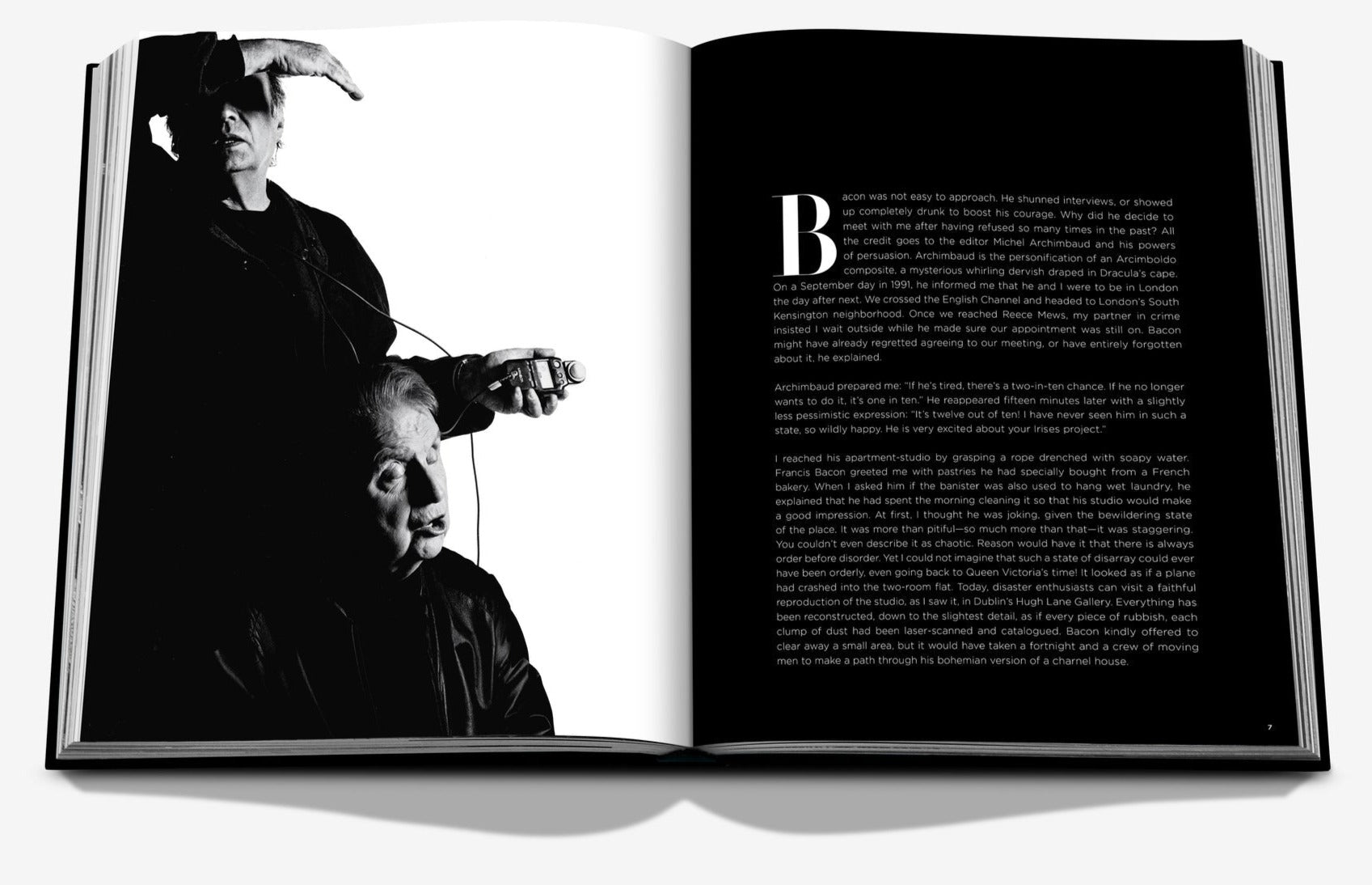 Open book displaying a black-and-white photograph of two people, one standing behind the other. The left page has a cropped image of a person and the right page contains text, reminiscent of the evocative exhibits at Marlborough Gallery or the haunting portraits by Francis Bacon from Assouline.