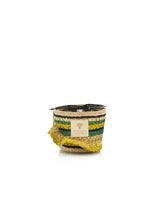 Baobab's Fety Milalao Candle is presented in a woven straw basket featuring green, yellow, and natural stripes. It's accentuated by a yellow cloth with mint freshness draped over one side, and a white label graces the front.