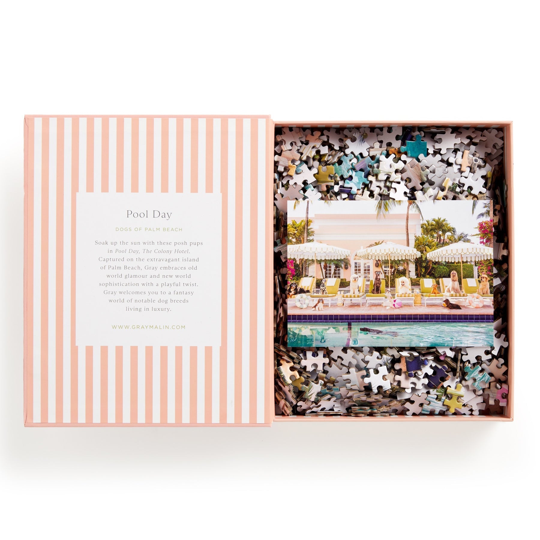 Open the Chronicle Books Gray Malin 1000 Piece Puzzle Book Box to reveal a partially completed Palm Beach Poolside puzzle, showcasing umbrellas, palm trees, and The Colony Hotel in a vibrant scene.