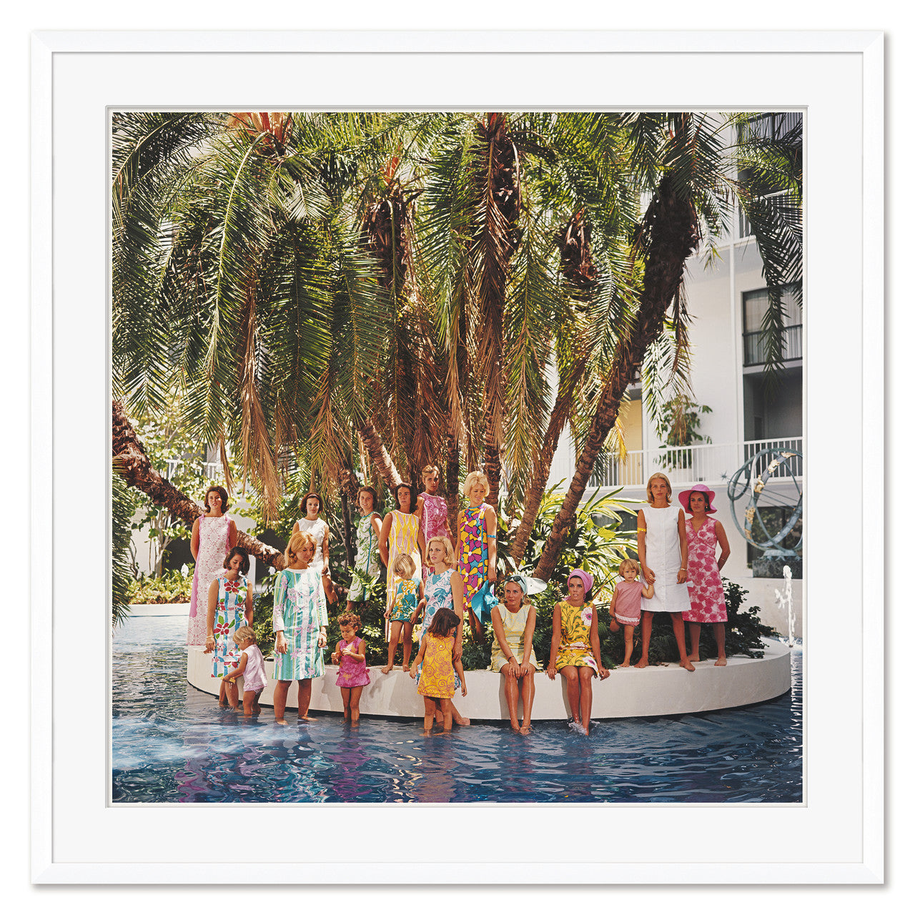 A group of people in vibrant attire pose on a circular platform surrounded by water and palm trees, echoing Slim Aarons' iconic photography in Getty Images' "Young Society," from April 1, 1964, offered by Soicher Marin.
