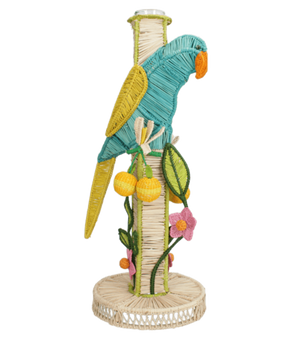The El Pajaro Flower Vase by Mercedes Salazar features a colorful woven parrot perched on a cylindrical, parrot-adorned container, decorated with vibrant yellow fruits and pink flowers for a lively tropical touch.