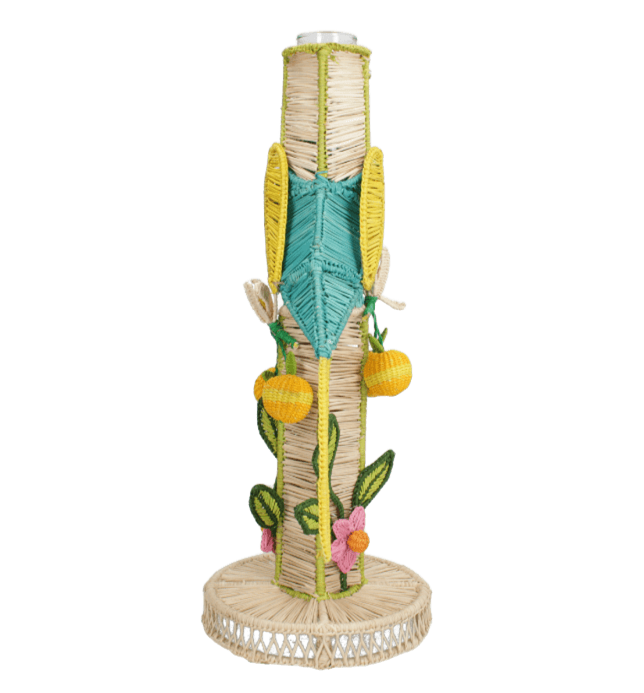 The El Pajaro Flower Vase by Mercedes Salazar features a tall, cylindrical design wrapped in straw and adorned with vibrant woven flowers, leaves, and fruit on a round base—ideal for bringing a tropical touch to any space.