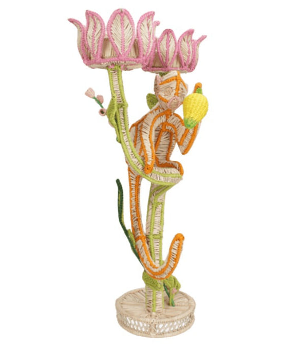 The El Mico Candle Holder by Mercedes Salazar features a woven rattan striped cat holding a yellow fruit, perched on a green stem below a pink and white flower—this whimsical piece brings playful charm to any space.
