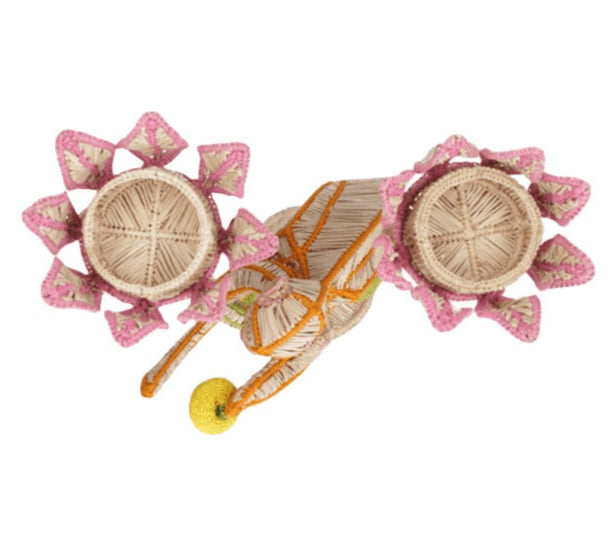The El Mico Candle Holder by Mercedes Salazar features woven straw and whimsical design, vibrant pink and green floral details, a yellow ball accent, and two wheels—making it a charming functional décor piece for any space.