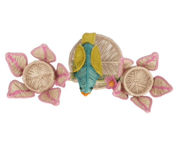 The El Loro Candle Holder by Mercedes Salazar adds tropical cheer with a central green and yellow parrot and vibrant natural and pink details, making it a charming raffia centerpiece for any space.