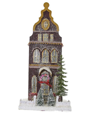 The Cody Foster Frosted Dutch House is a tall, brown, glittery decorative cardboard building with arched windows, snowy accents, wreath, and small trees—measuring 8x8x18 inches and evoking a charming winter holiday scene.