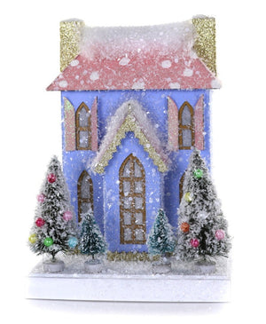 The Cody Foster Petite Blue/Pink House is a small cardboard décor featuring a blue house with pink roof, gold details, snow, and four festive Christmas trees in front. Refer to product dimensions for exact size details.