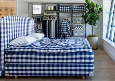 interior of Hastens Palm Beach with blue and white check Hastens bed and shelving in the background with various Hastens accessories