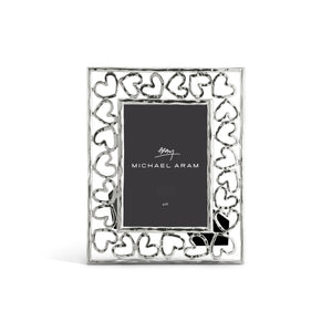 The Michael Aram Heart Frame Collection features a silver picture frame with a border of interconnected hearts, highlighting love and craftsmanship, and includes a "Michael Aram 4x6" placeholder card.