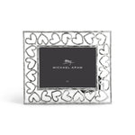 A silver photo frame from the Heart Frame Collection by Michael Aram features a heart-patterned border and a branded placeholder card, celebrating handcraftsmanship and love in every detail.