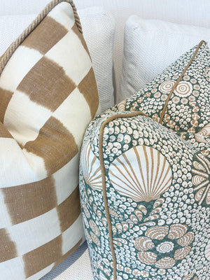 Two decorative throw pillows rest on a light couch: the Checkerboard Toffee Pillow from Hive Custom Pillows with a tan and white checkered pattern, and another pillow featuring a green and beige floral design.