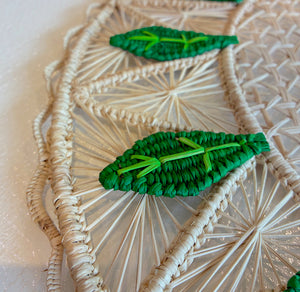 Close-up of the Mil Hojas Placemat by Mercedes Salazar, handwoven from cream raffia and adorned with textured green leaf designs.