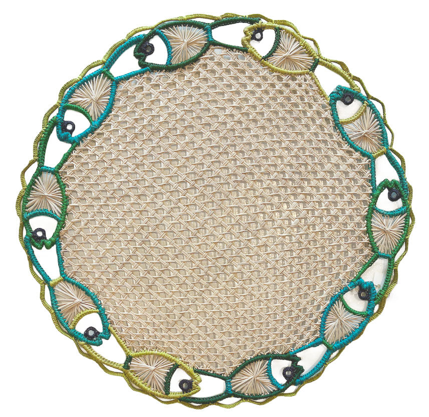 The Mercedes Salazar Fish Dance Placemat is a round woven placemat with an embroidered border of fish and seashell motifs in green, blue, and beige, bringing ocean-inspired color and style to your table.