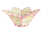 The Mercedes Salazar Pink Petals Basket is a woven raffia basket with five petal-shaped sections and pink trim, ideal for displaying tropical leaves.