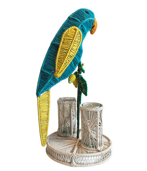 The Lemon Tree Flower Vase by Mercedes Salazar features a blue and yellow woven rattan parrot perched beside two cylindrical containers on a round base, bringing tropical charm to any centerpiece.