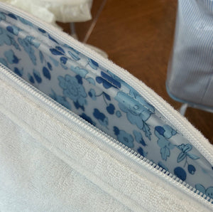 Close-up of the Large Shell Toiletry Bag in Sand by Weezie Towels, featuring a blue floral-patterned interior lining and a handy pocket, displayed on a wooden surface.