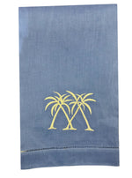 A blue hand towel from the Pink House Mustique Coastal Linen Hand Towel Collection with two embroidered yellow palm trees near the bottom center, bringing seaside charm to your dining space.