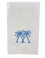 The Coastal Linen Hand Towel Collection by Pink House Mustique features a white linen towel with two pairs of blue embroidered palm trees, perfect for adding subtle seaside charm and relaxed coastal style to your table setting.