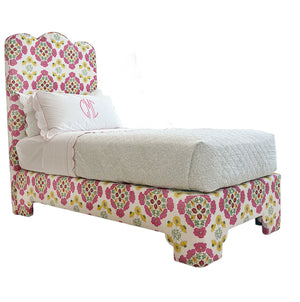The EJ Schrader Rosa Spring Twin XL Bed is a playful bedroom piece with a floral-patterned upholstered frame and headboard, paired with white bedding and a quilted blanket.