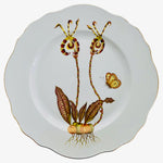 A hand-painted white porcelain dinner plate from Anna Weatherley's Orchid I Dinnerware Collection features wavy edges and a botanical illustration of pitcher plants, leafy stems, roots, and a butterfly on one side.