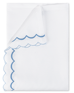 A folded white towel from the Matouk India Pique Bedding Collection in Azure features delicate double-scallop embroidery along the edges.