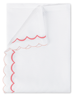 A neatly folded napkin from the Matouk India Pique Bedding Collection in Blush, featuring a white textured cotton blend with diamond pique and pink and red double-scallop embroidery.