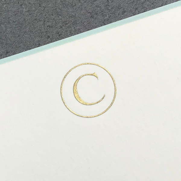 A gold copyright symbol is embossed on white paper with an aqua border, echoing Printery's elegant Initial Card Set, shown here with a gray background edge.