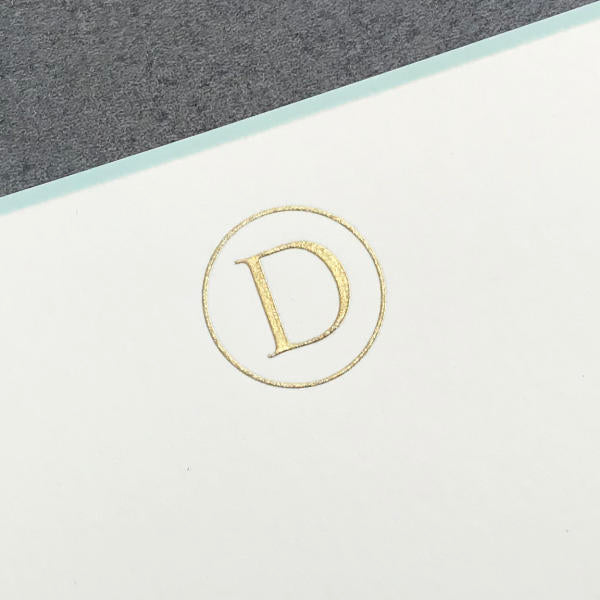 The Printery Initial Card Set features a gold letter "D" in a circle, embossed on a white surface with an elegant aqua border, set against a gray background.