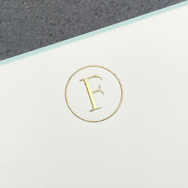 Printery's Initial Card Set features a gold "F" embossed in a circle on a white note card over a gray background—ideal for pairing with hand-lined envelopes or adding an aqua border for added elegance.