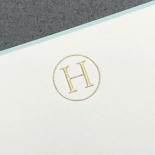 The Printery Initial Card Set features a gold letter "H" in a circle embossed on white paper with a gray top, paired with hand-lined envelopes for an elegant touch.