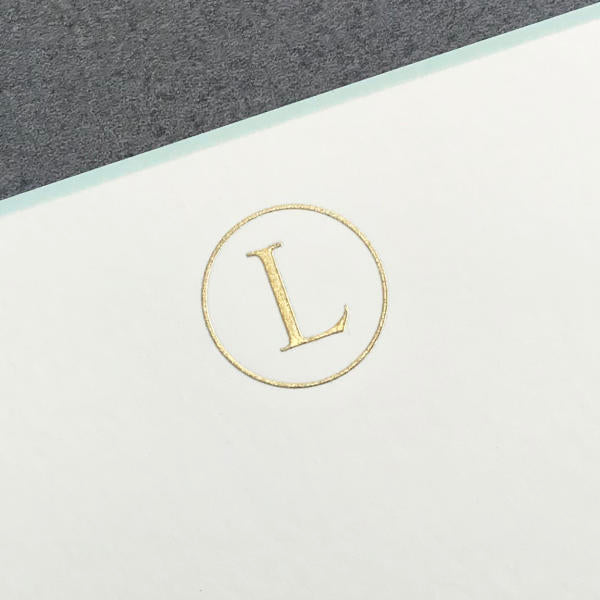 A gold initial "L" is centered in a circle on white, echoing the elegance of Printery's Initial Card Set note cards, with a gray background in the upper left corner.