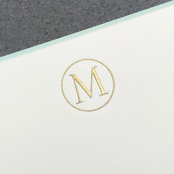 The Printery Initial Card Set features a gold letter "M" centered in a gold circle on white, accented by a gray top band for contrast—an elegant, timeless design inspired by classic gold initial note cards.