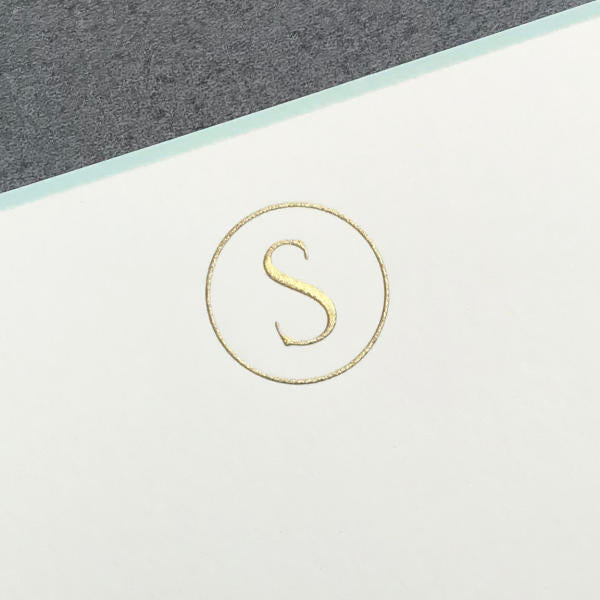 The Printery Initial Card Set features a gold "S" in a circle, centered on a white card with an aqua border and grey background. Each note card comes with a hand-lined envelope for an elegant finishing touch.
