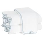 Two folded white towels with light blue trim from the Matouk Jasper Bath Collection, featuring a subtle scalloped silhouette, are stacked on a plain white background.