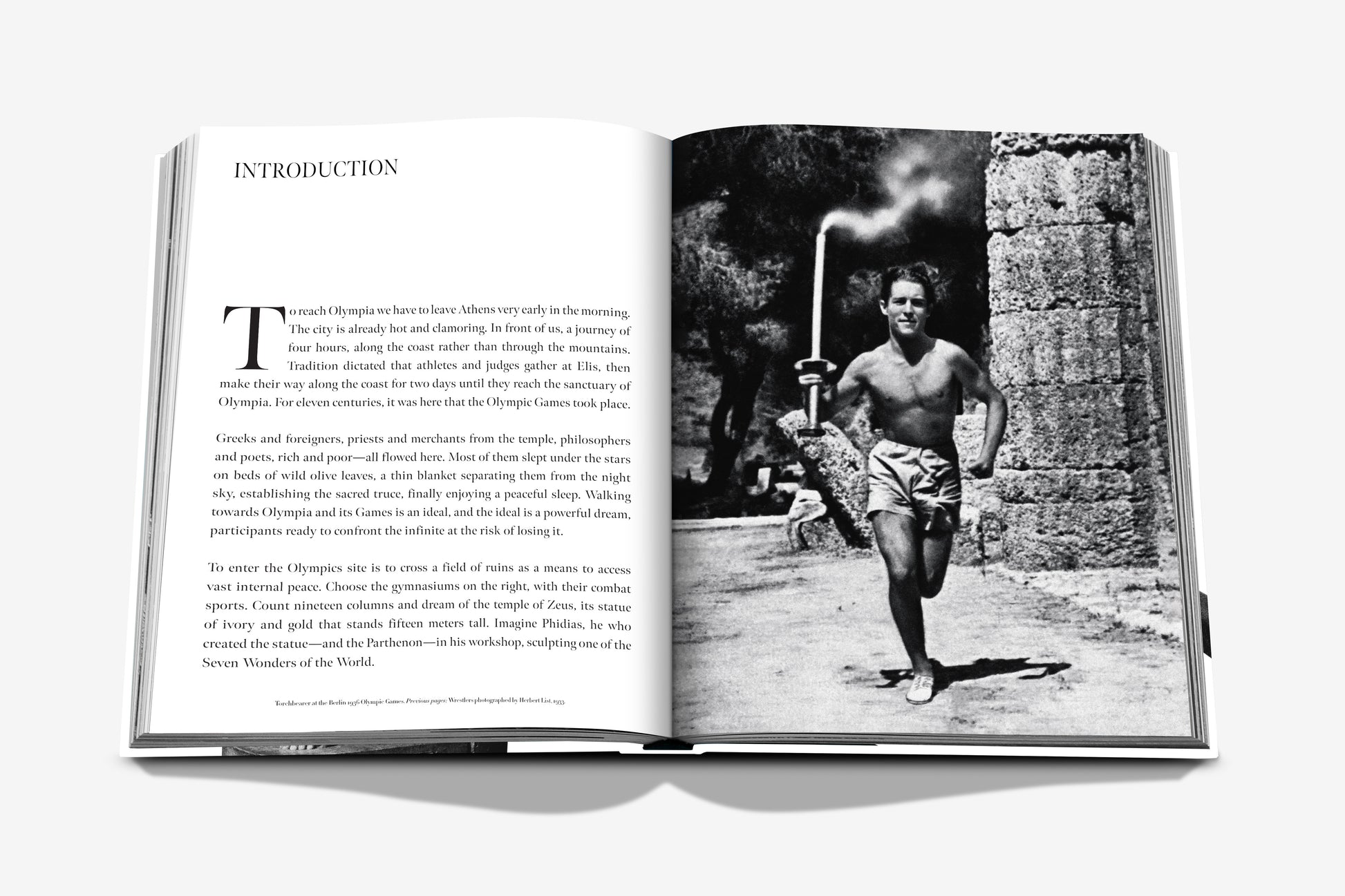 Open book displaying a page with the heading "INTRODUCTION" on the left and a black-and-white photo of a shirtless man carrying a torch from the Summer Olympics history on the right, featured in "The Last Heroes: 100 Moments of Olympics Legend" by Assouline.