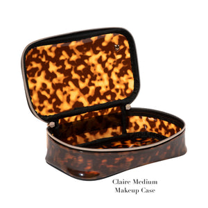 An open, see-through makeup case from the Stephanie Johnson Miami Tortoise Travel Collection features a brown tortoiseshell pattern, faux-leather trim, and zipper closure. Displayed on a white background. Text reads "Claire Medium Makeup Case.