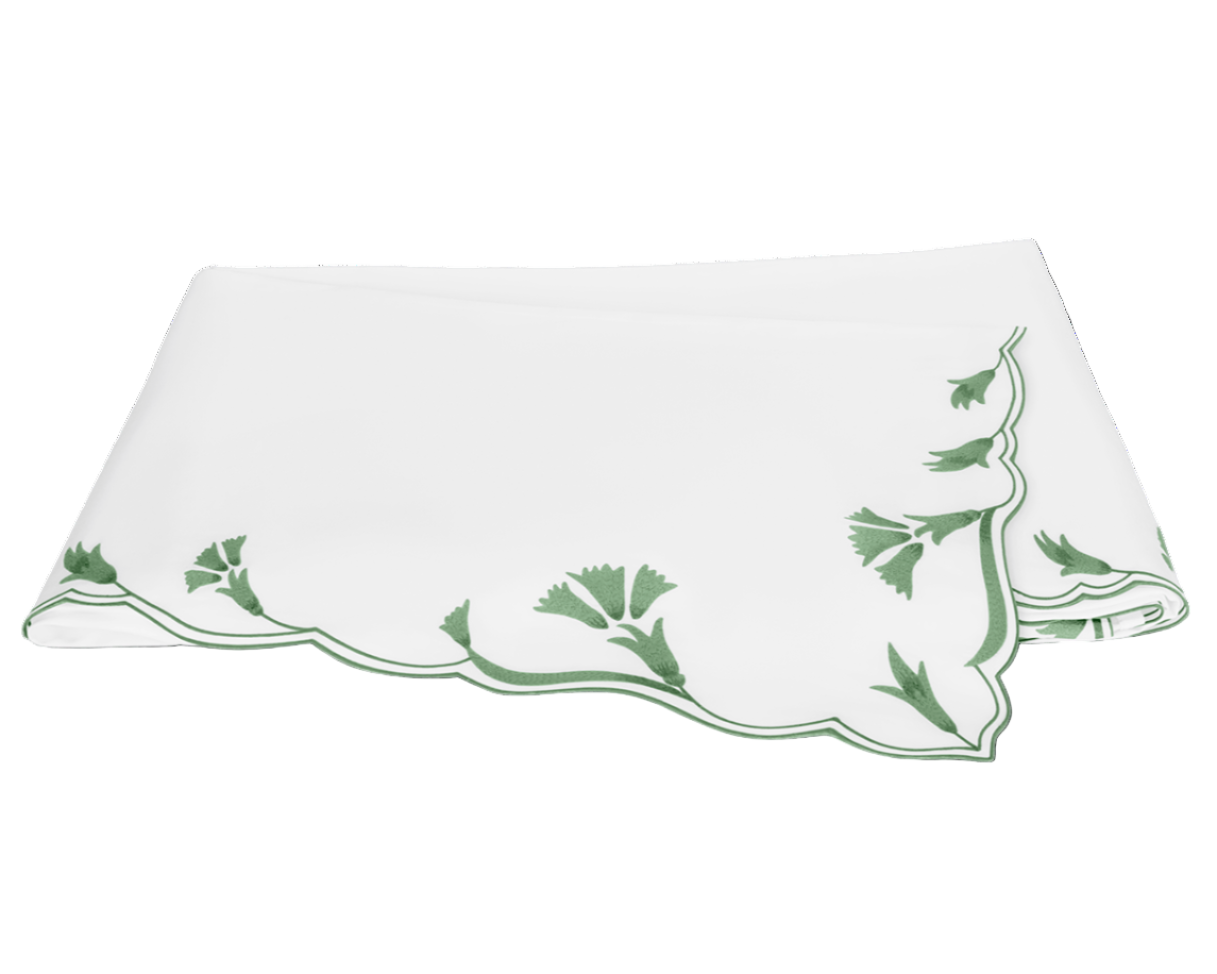 A folded white tablecloth with scalloped florals and green embroidery along the border, reminiscent of the Marcella Bedding Collection, Clover by Matouk.