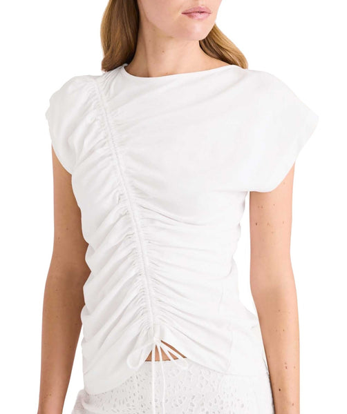 A woman wearing a white Merlette New York organic cotton Merlette Reverie Jersey Top with an adjustable ruched front and an asymmetrical sleeve design.