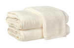 Two neatly folded, absorbent Matouk Milagro Bath Collection towels in ivory are stacked on top of each other against a white background.