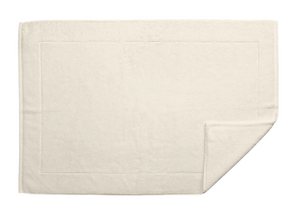 A Matouk Milagro Bath Collection towel in ivory is laid flat with a corner folded over, highlighting its soft texture, absorbent cotton, and simple border design.