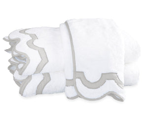 Two folded white towels from the Matouk Mirasol Bath Collection feature decorative scalloped edges trimmed in light gray and are stacked on a white background.