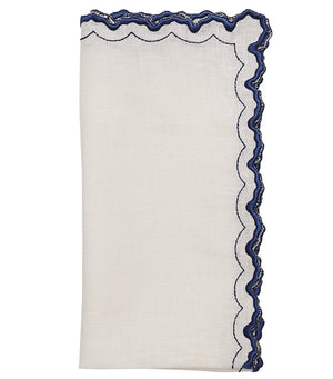 The Arches Napkin Set by Kim Seybert features folded white linen napkins with dark blue scalloped, embroidered edges and a subtle geometric design.