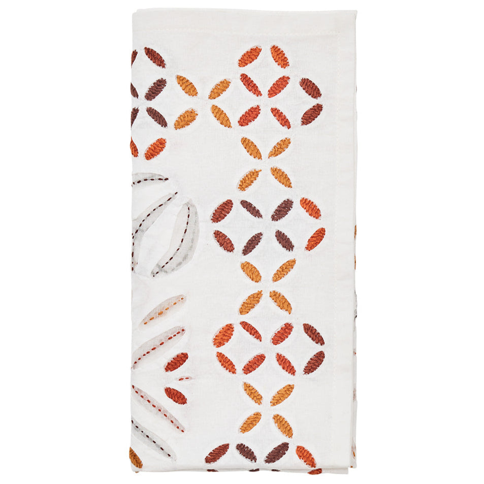 The Kim Seybert Malta Napkin Set features white napkins with embroidered red, orange, and brown leaf patterns and cutwork-inspired cut-out details along one side.